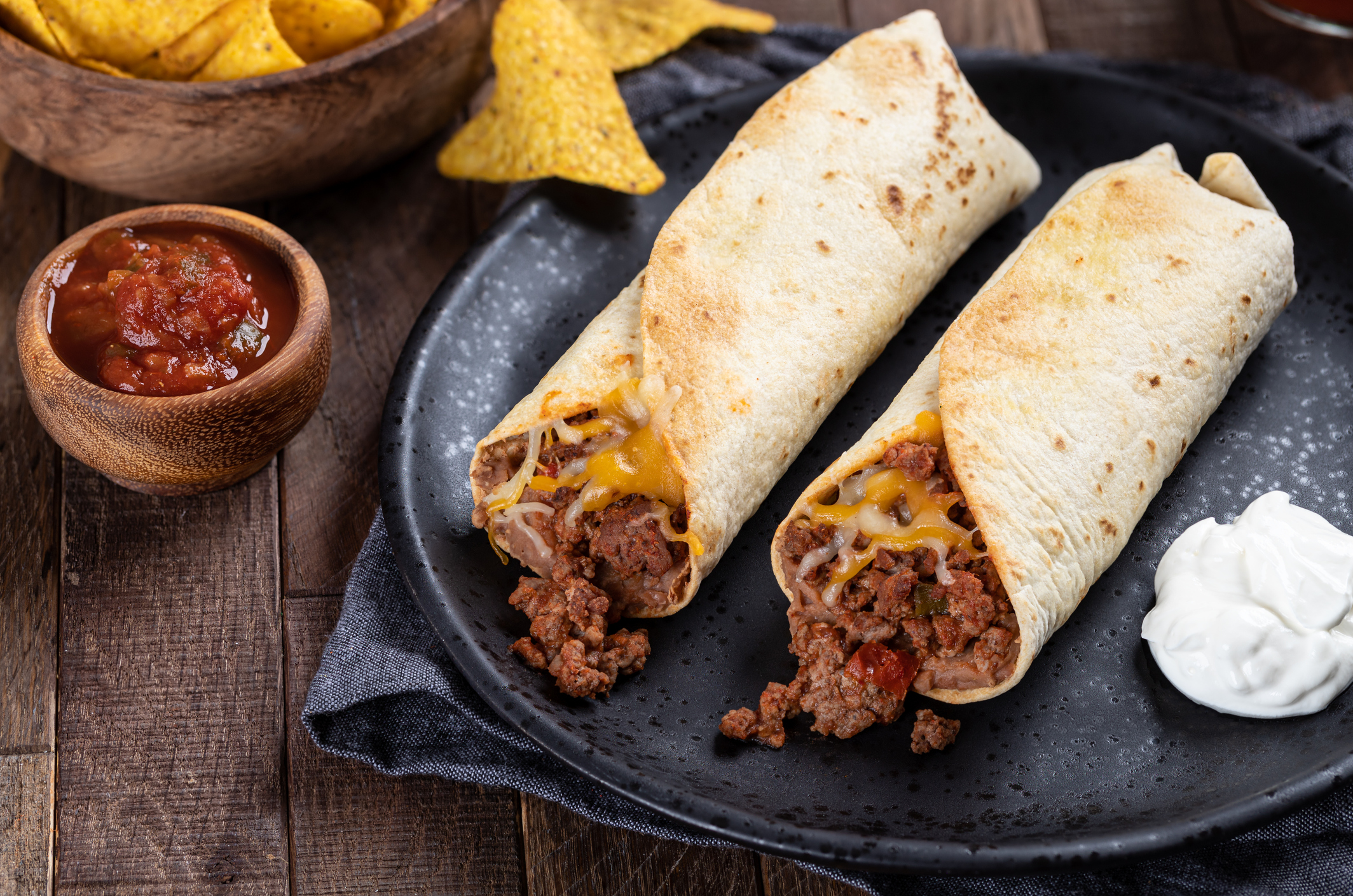 Burritos with ground beef, refried beans and cheese on a black plate with salsa and tortilla chips