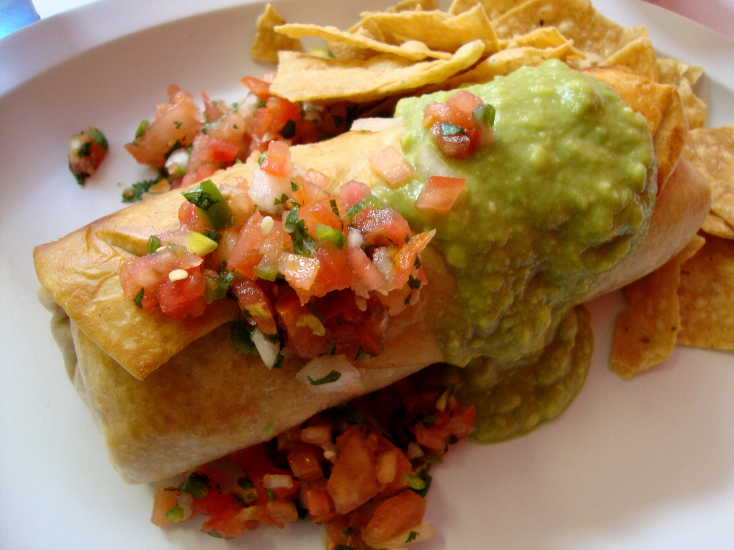 Chimichanga with guacamole, and Salsa on top and a side of chips.