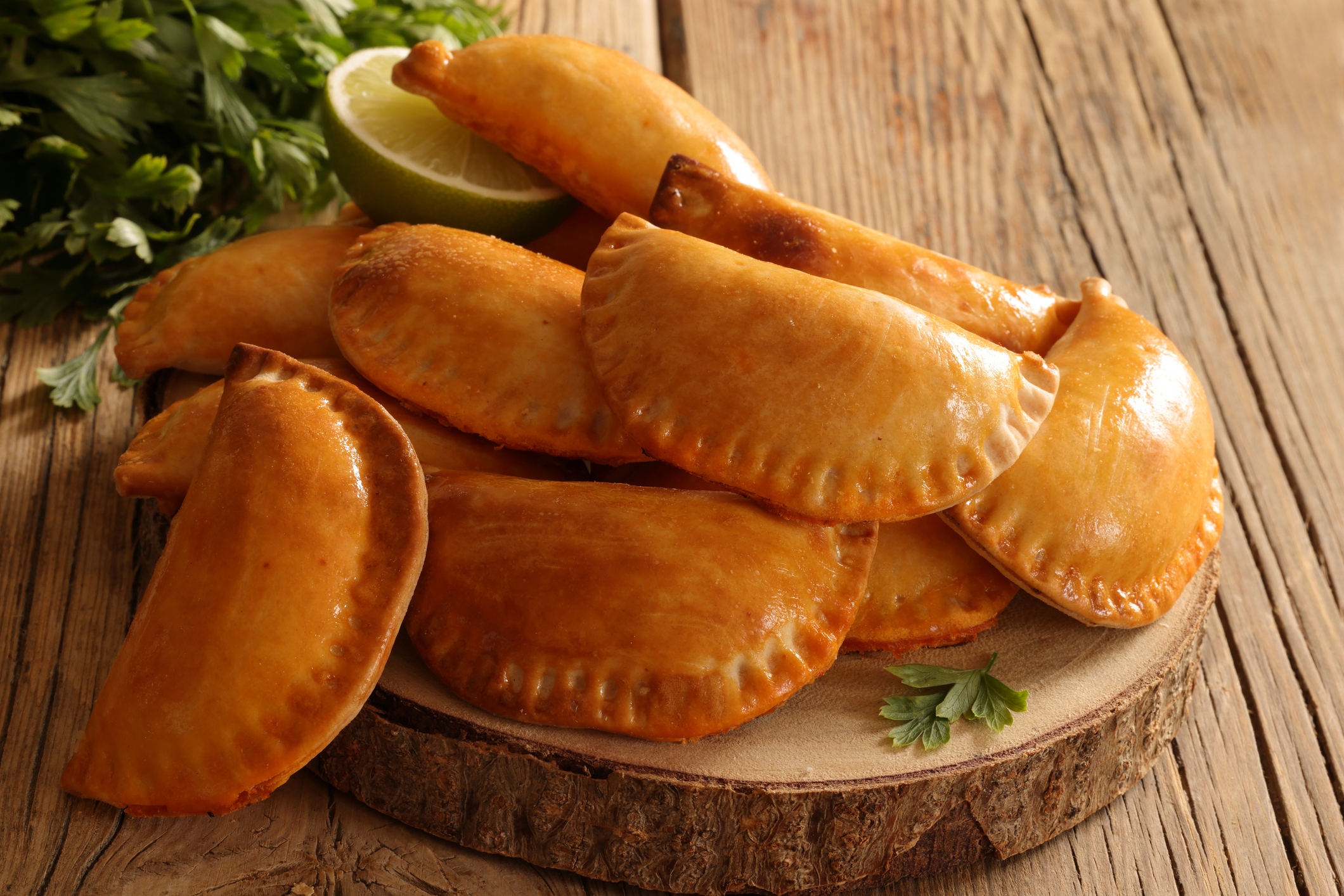 Empanadas or miniature Cornish Pasties with meat and chili sauce, coated with egg yolk giving a distinctive glaze on wood background. High resolution image 45Mp using Canon EOS R5 and associate macro lens