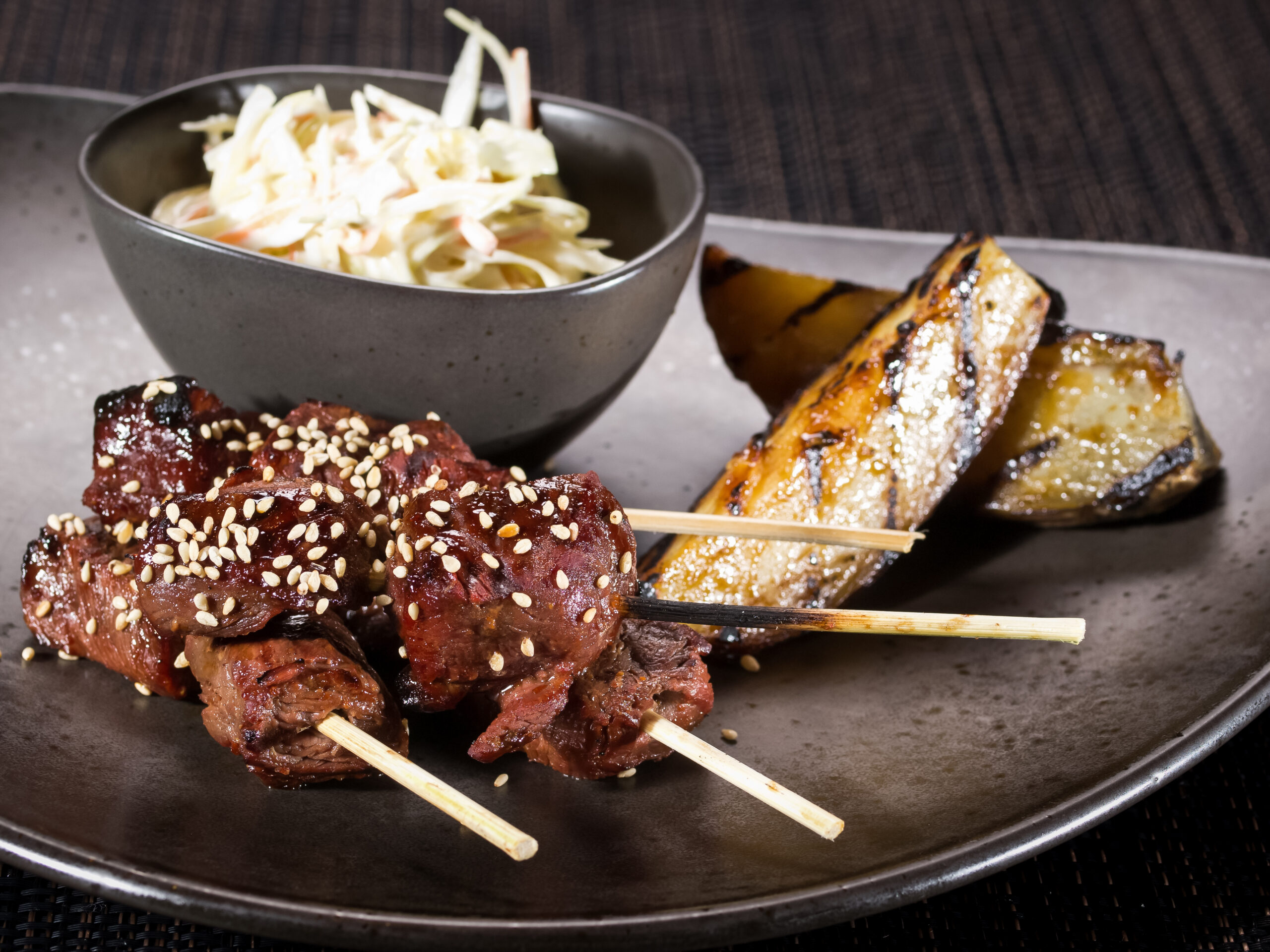 portion of grilled beef fillet skewers with salad coleslaw and grilled potato on a plate on dark background, horizontal photo