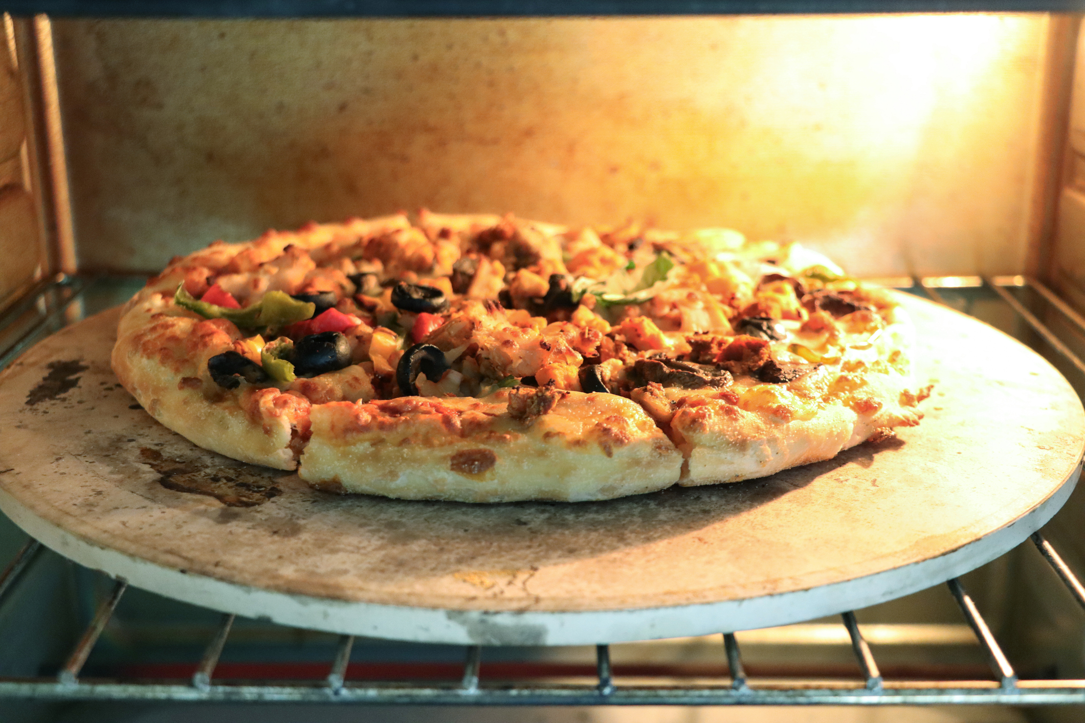 Stock photo showing baked, homemade vegetables and black olive pizza recipe with freshly made dough and tomato sauce topping, cooked on pizza stone, for a crispy base, in a hot oven.