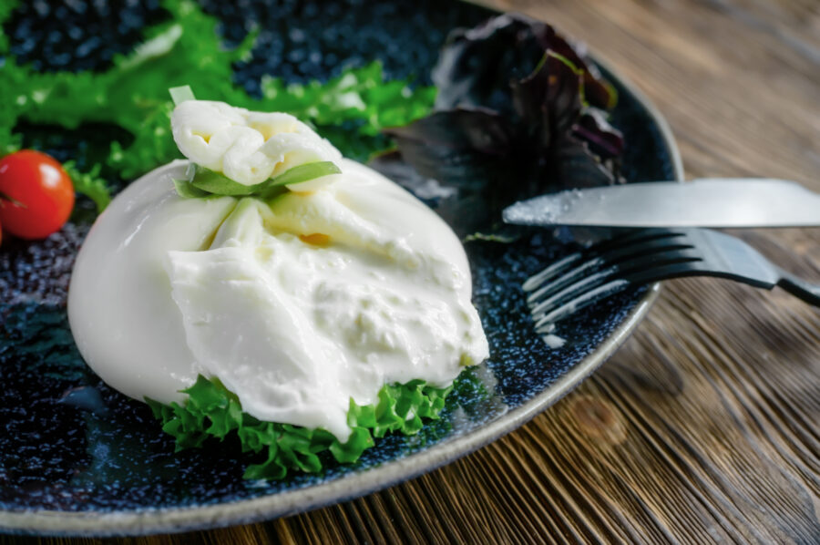 Burrata on a dark plate with tomatoes and arugula. Close-up