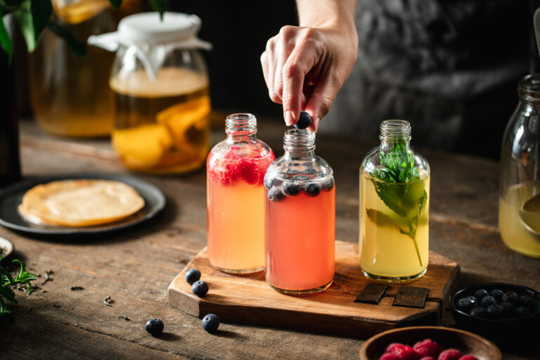 Cropped shot of woman preparing blueberry, raspberry, and mint kombucha tea in kitchen table.