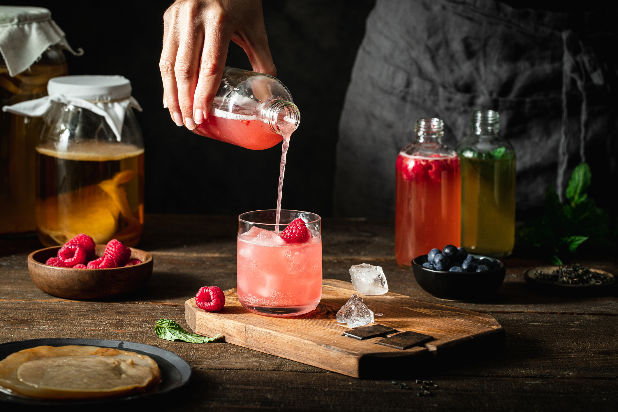 Close-up of woman pouring raspberry kombucha tea in glass from bottle.