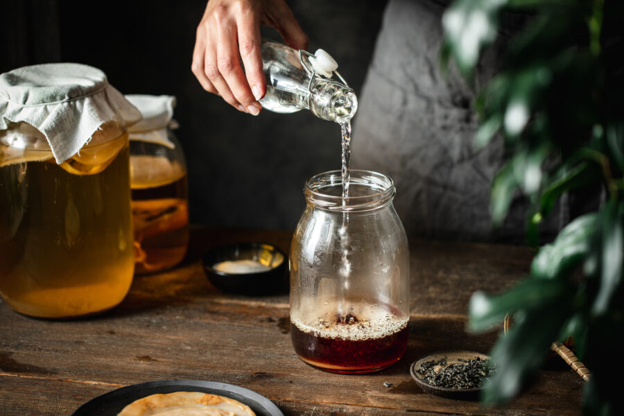 Woman hand pouring water in black tea jar for making kombucha in kitchen.