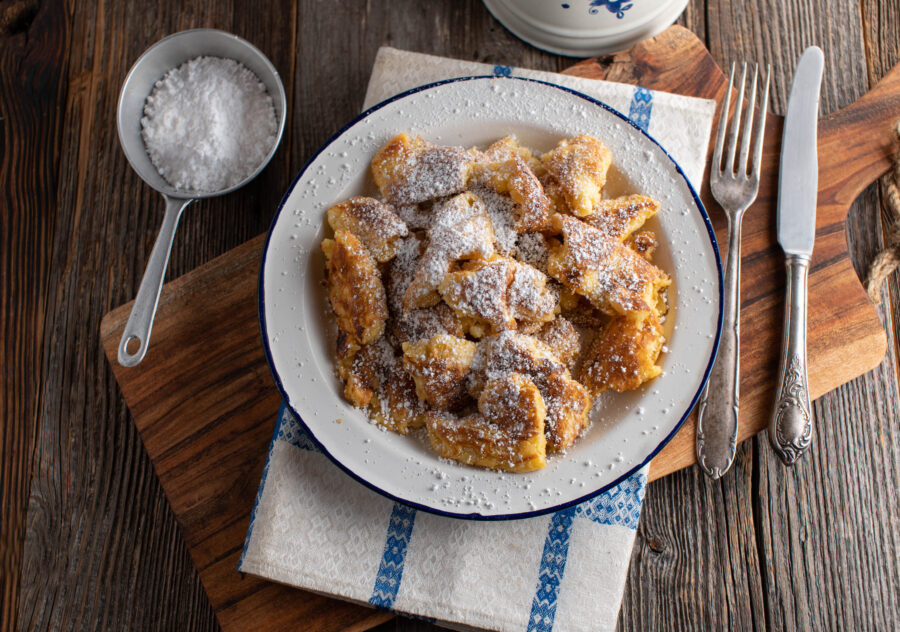 Traditional austrian pancake "Kaiserschmarrn" with powdered sugar topping. Served on a old fashioned plate on rustic and wooden table background. Top view with copy space