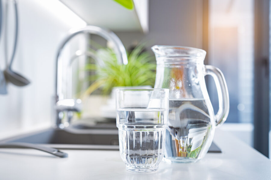 Close up of a glass of water and a jug on kitchen counter.