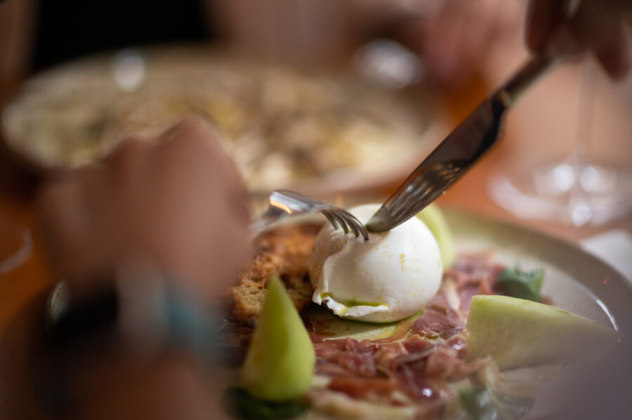 Woman hands cutting burrata cheese on a beef carpaccio in an Italian restaurant.