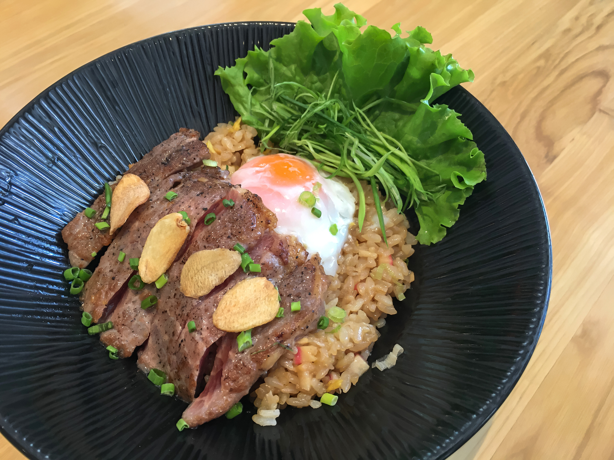 Close-up shot Gyudon (Japanese Beef Rice Bowl) With Egg. There's slices of medium rare beef steak and fried garlic on top.