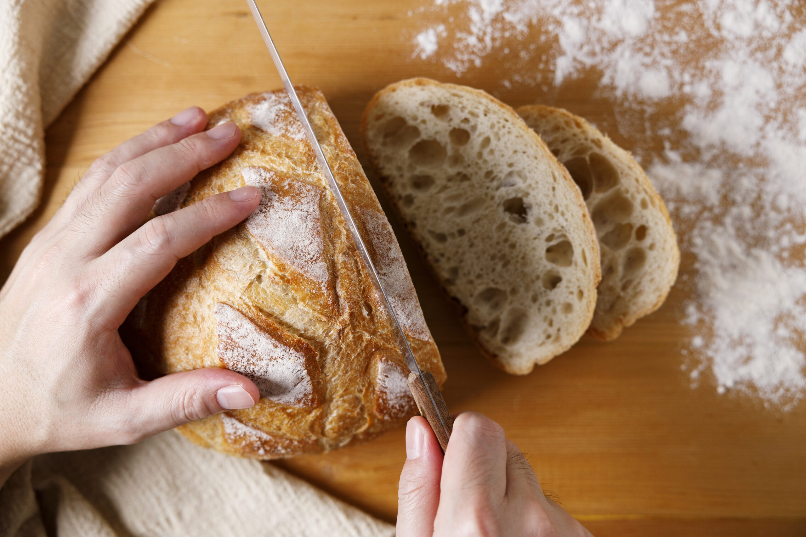 Baker or chef holding freshly made bread. Fresh sourdough bread with a golden crust on wooden table. Top view.