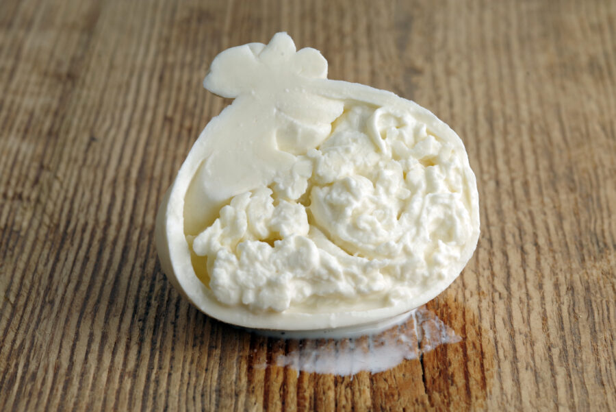 Sliced head of typical Italian cow milk cheese Burrata on a wooden background. Selective focus.