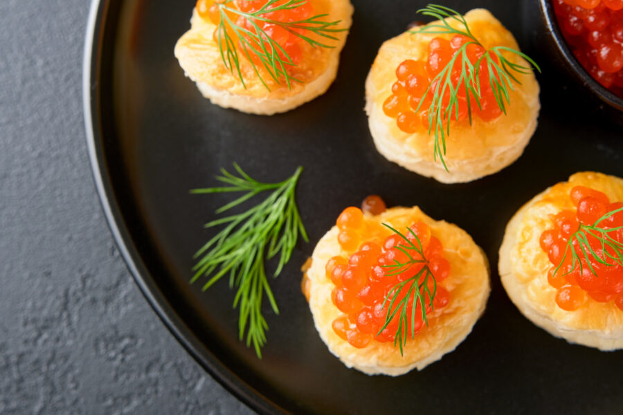 Salmon red caviar toast on black plate. Gray background.