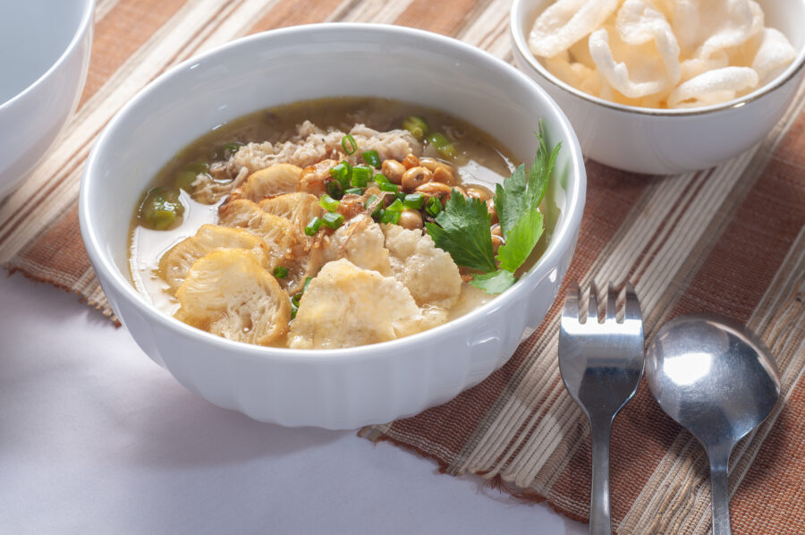 Bubur Ayam Sukabumi contains white rice porridge with side dishes of fried chicken slices, fried soybeans, emping crackers and sprinkled with fried onions and celery