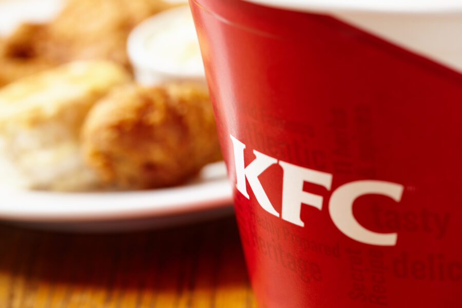 close-up of a KFC bucket, with a plate of chicken in the background