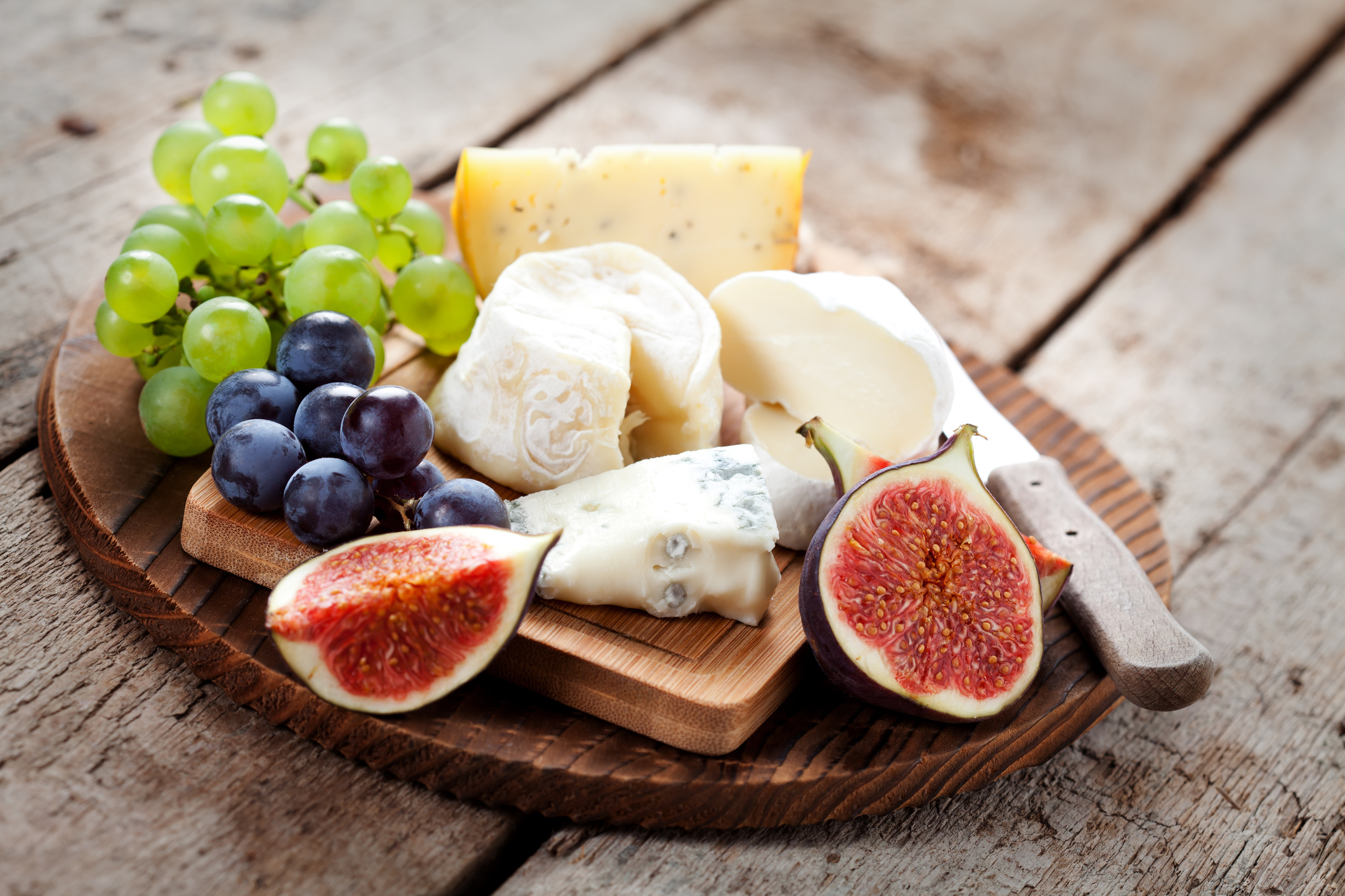 variety of cheeses on wooden plate with fruits