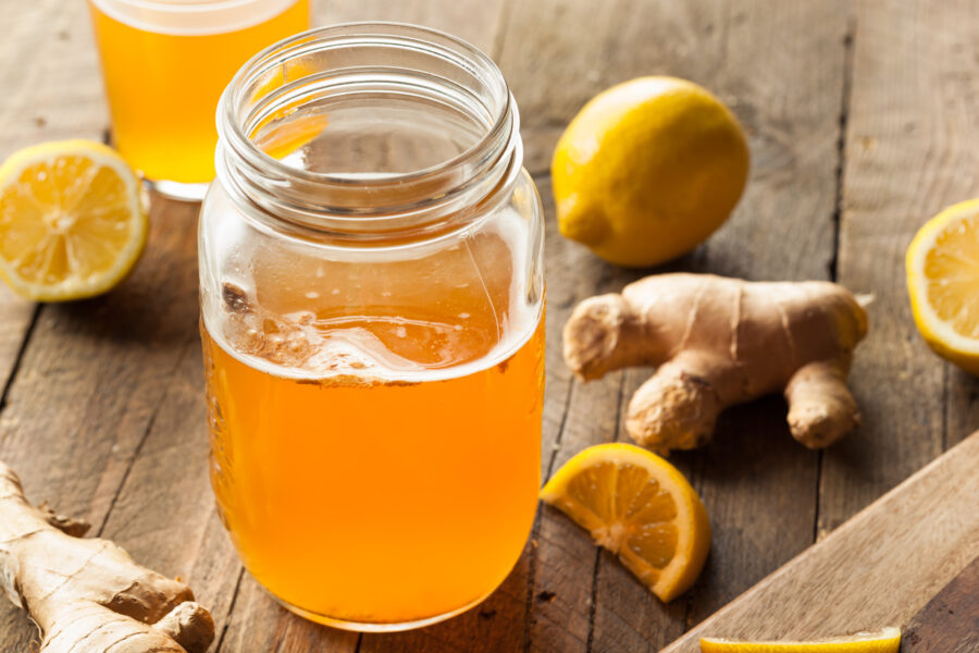 glass mason jar filled with kombucha, surrounded by ginger roots and lemons