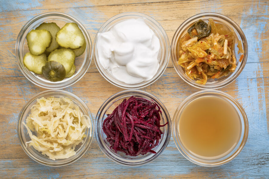 a set of fermented food - top view of glass bowls against grunge wood:  cucumber pickles,  coconut milk yogurt, kimchi, sauerkraut, red beets, apple cider vinegar
