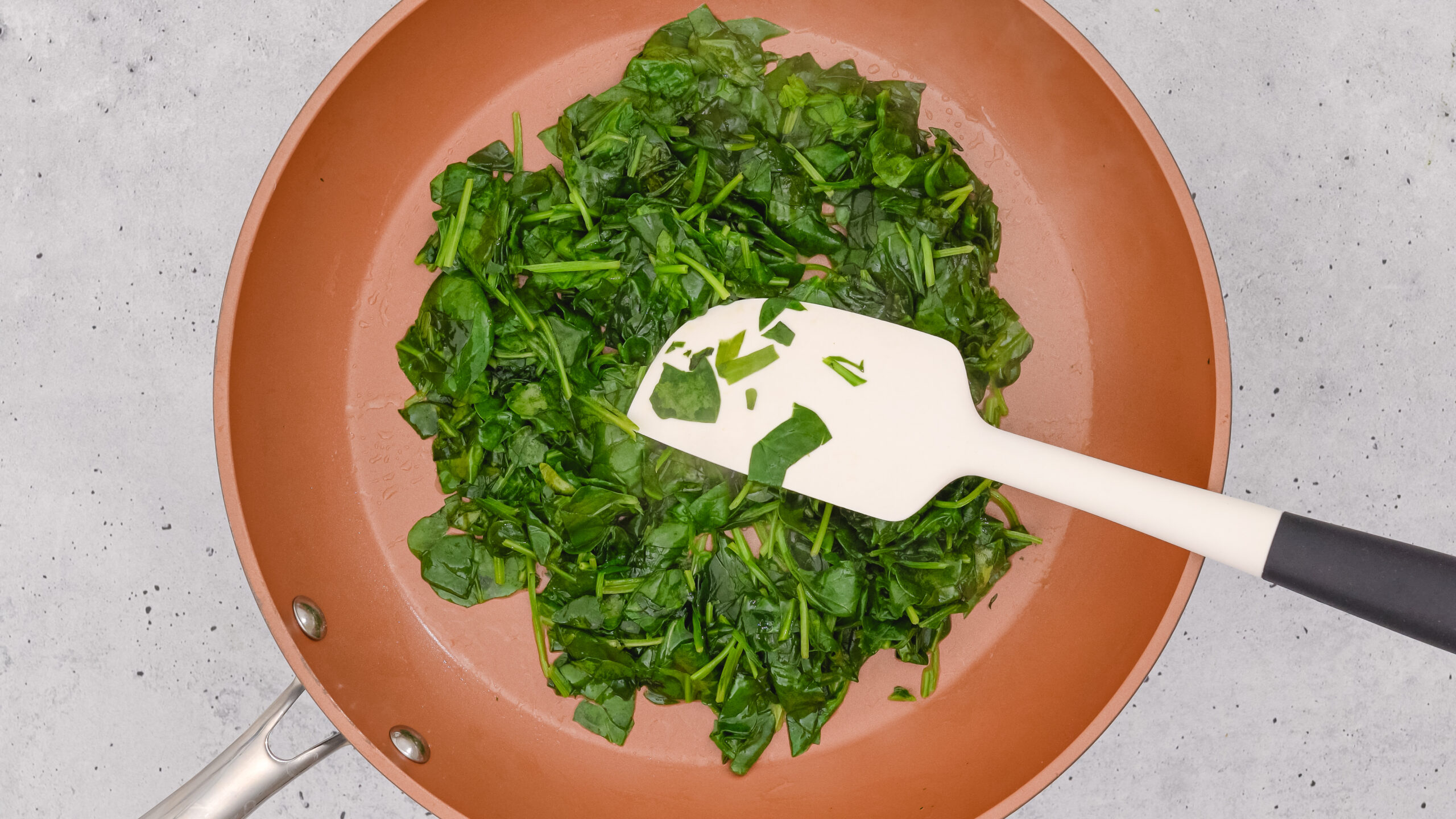 Mixing baby spinach on a frying pan. Close up view from above, copy space