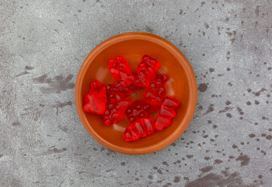 Overhead view of a small bowl of colorful red gummi bear sugar candies on a gray mottled background.