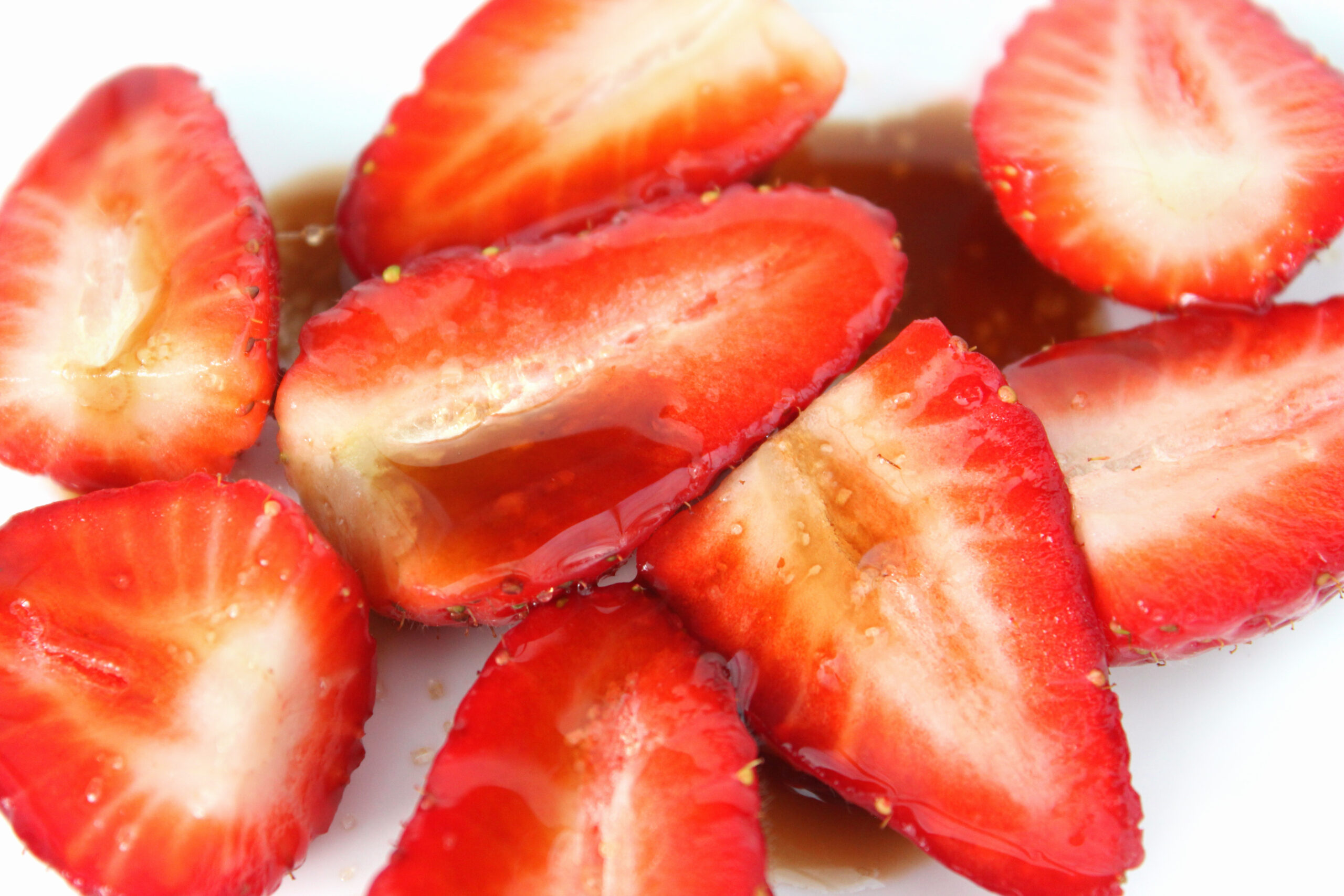 Photo showing a dish of sliced strawberries, which have been drizzled with balsamic vinegar and sprinkled with a little brown sugar.  Strawberries with balsamic vinegar is considered to be something of a 'gourmet dessert' way to eat these tasty, juicy summer fruit berries, helping to enhance the flavour.