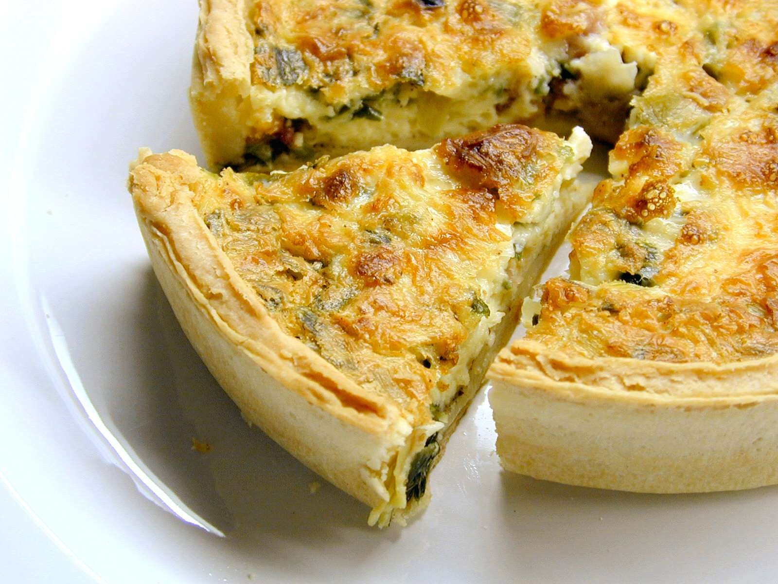 Pie of quiche on white plate.