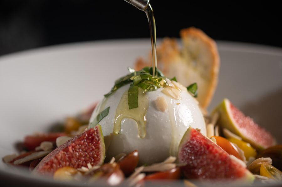 Pouring olive oil on a salad with burrata and fig slices.