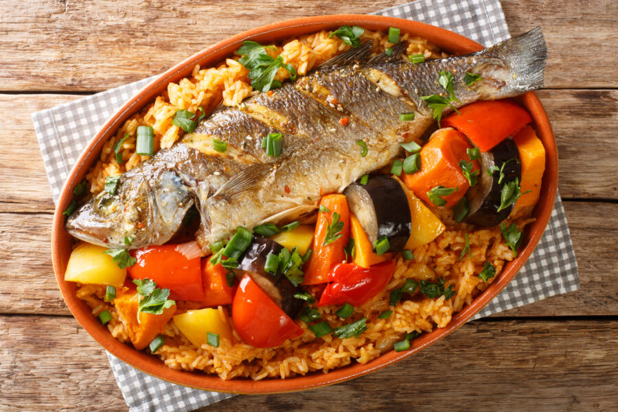 Senegalese Thieboudienne: fresh fish, and rice, cooked with vegetables such as cassava, pumpkin, cabbage, carrot, eggplant closeup on the table. horizontal top view from above