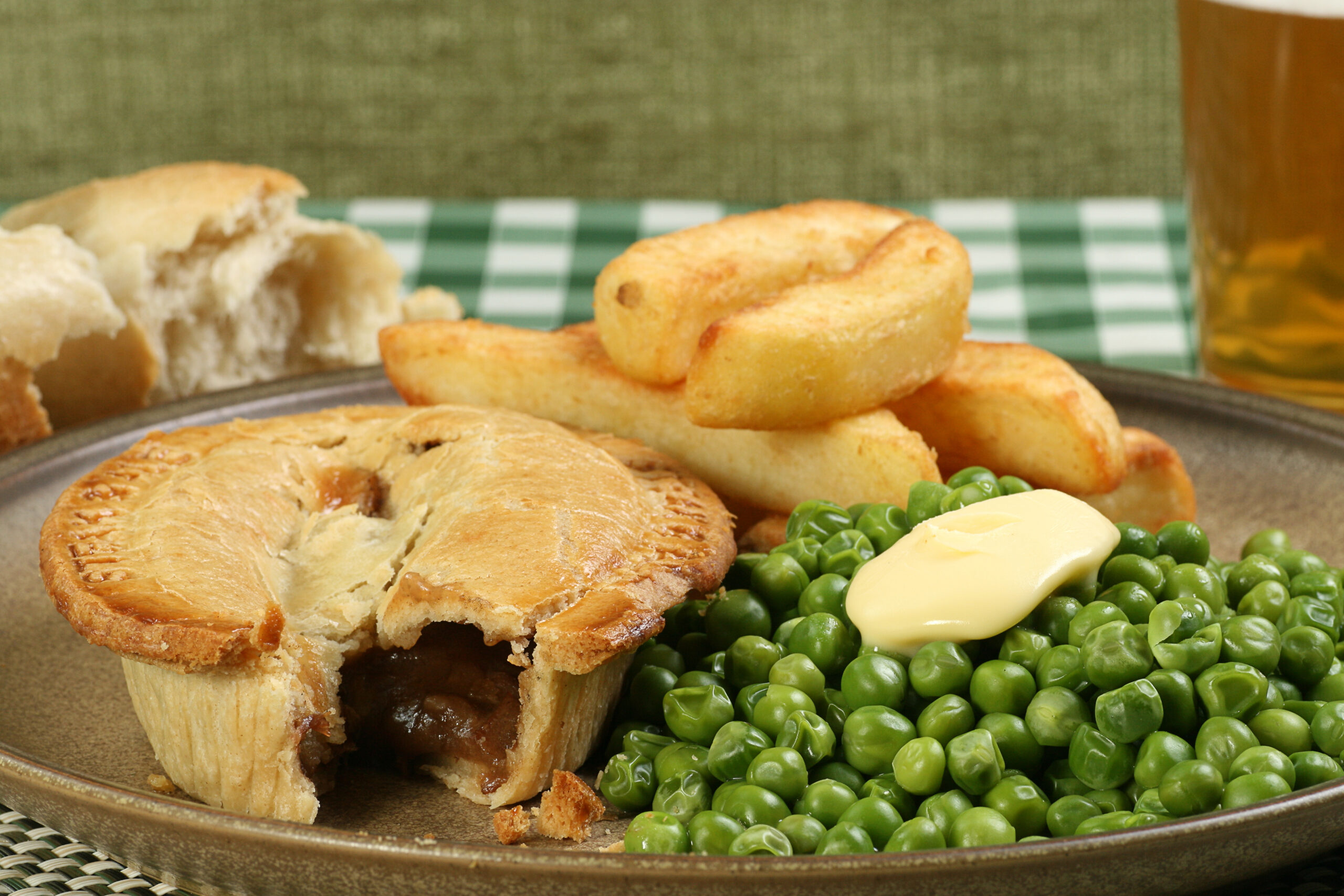 Steak and ale pie on a rustic plate with fries and peas