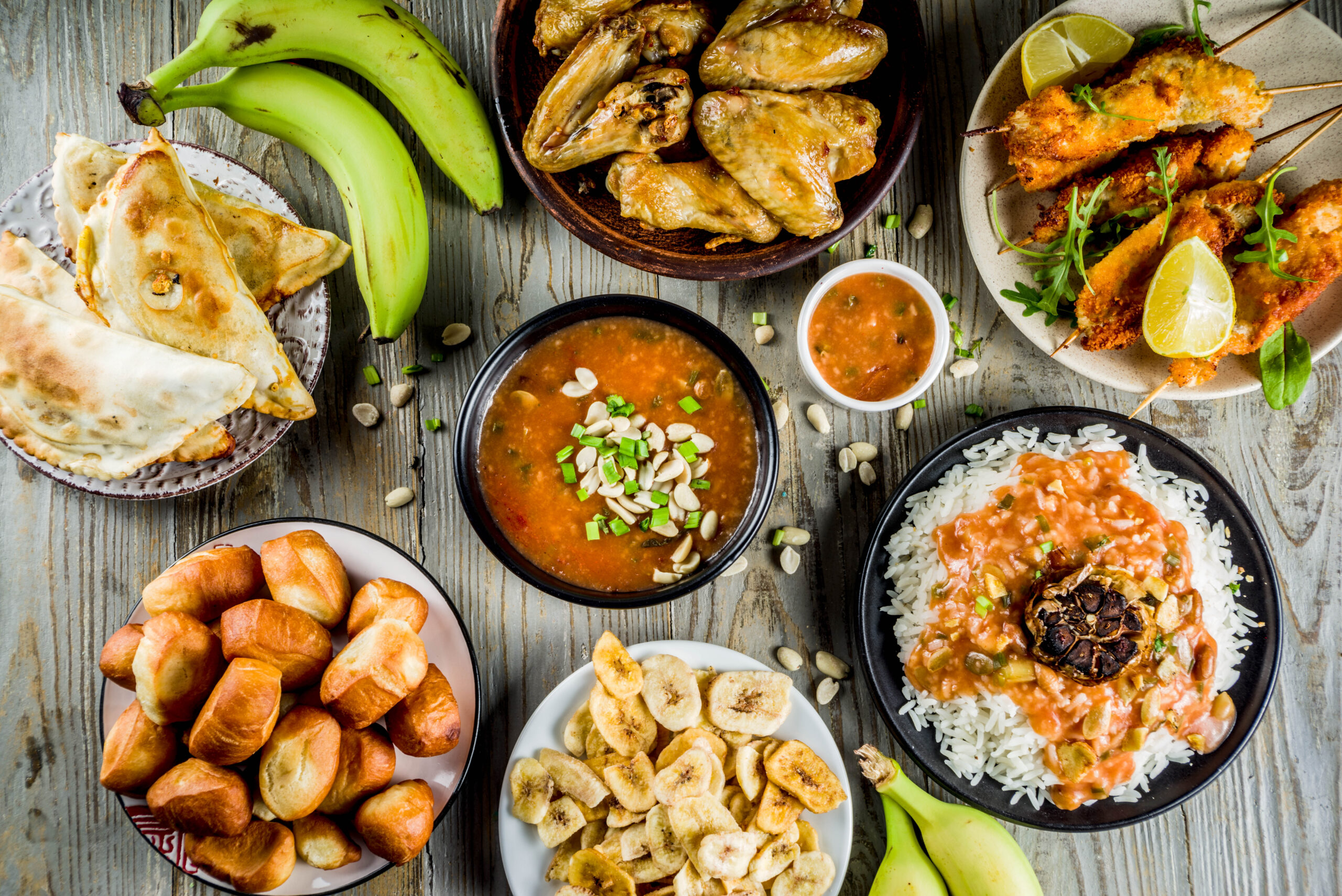 Traditional Wset African dishes assortment - peanut soup, jollof rice, grilled chicken wings, dry fried bananas plantains, nigerian chicken kebabs, meat pies, top view