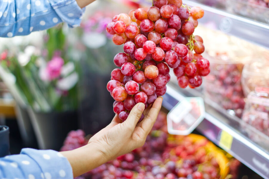 Woman choosing bunch fresh red grape to buy in supermarket