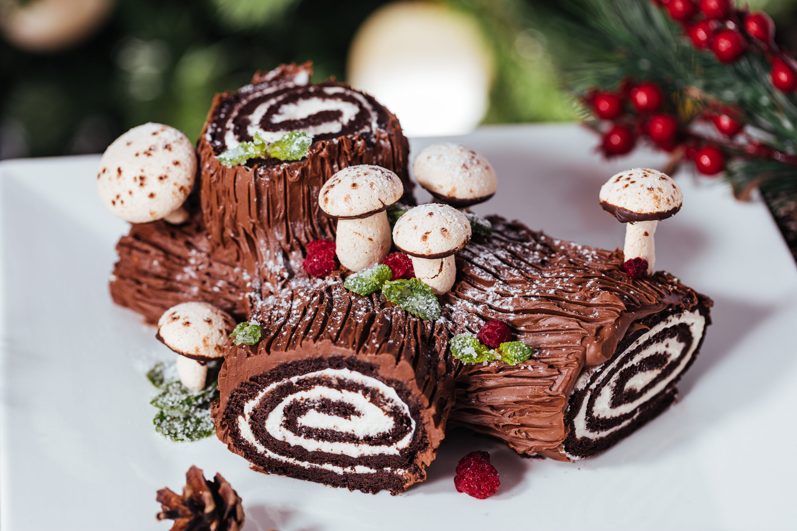 Yule log or Bûche de Noël cake on white plate in front of Christmas tree