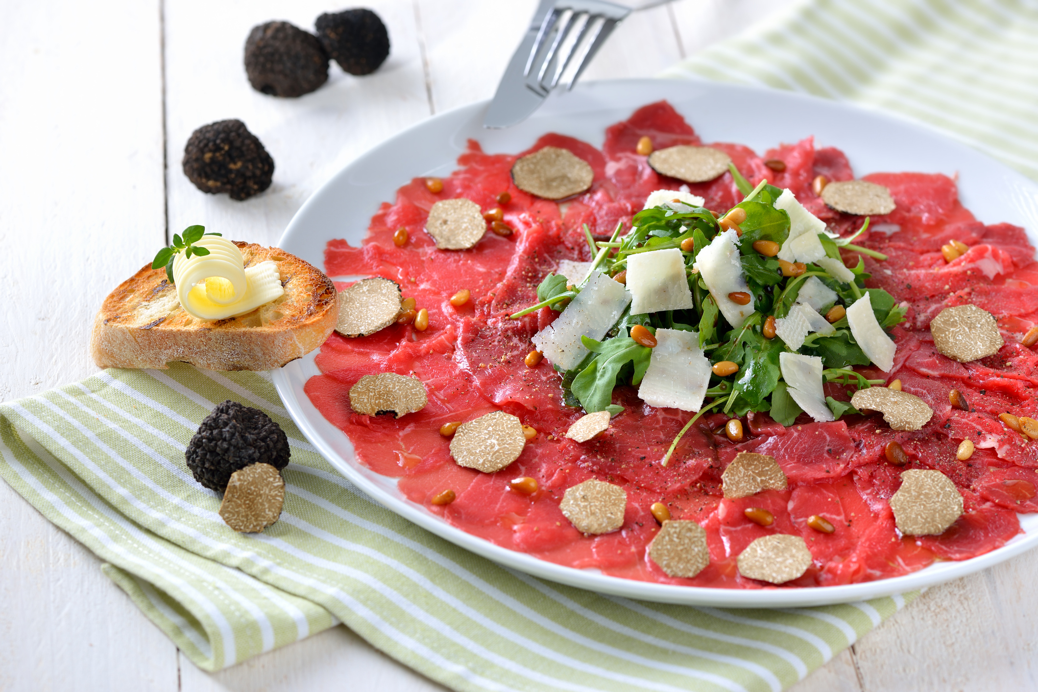 Carpaccio of beef fillet with sliced black truffles, rocket salad with parmesan cheese and roasted pine nuts, served with a slice of toasted baguette with a butter roll