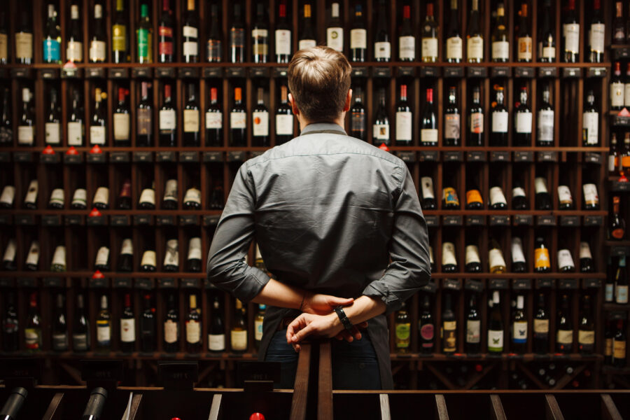 Bartender at wine cellar full of bottles on large wooden shelves.