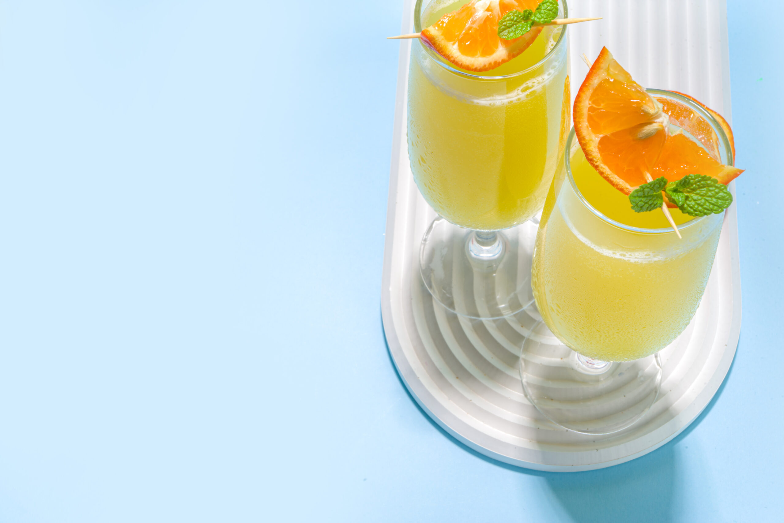 Classic summer mimosas cocktail, with orange juice, on  light blue background. Summer bar menu concept copy space