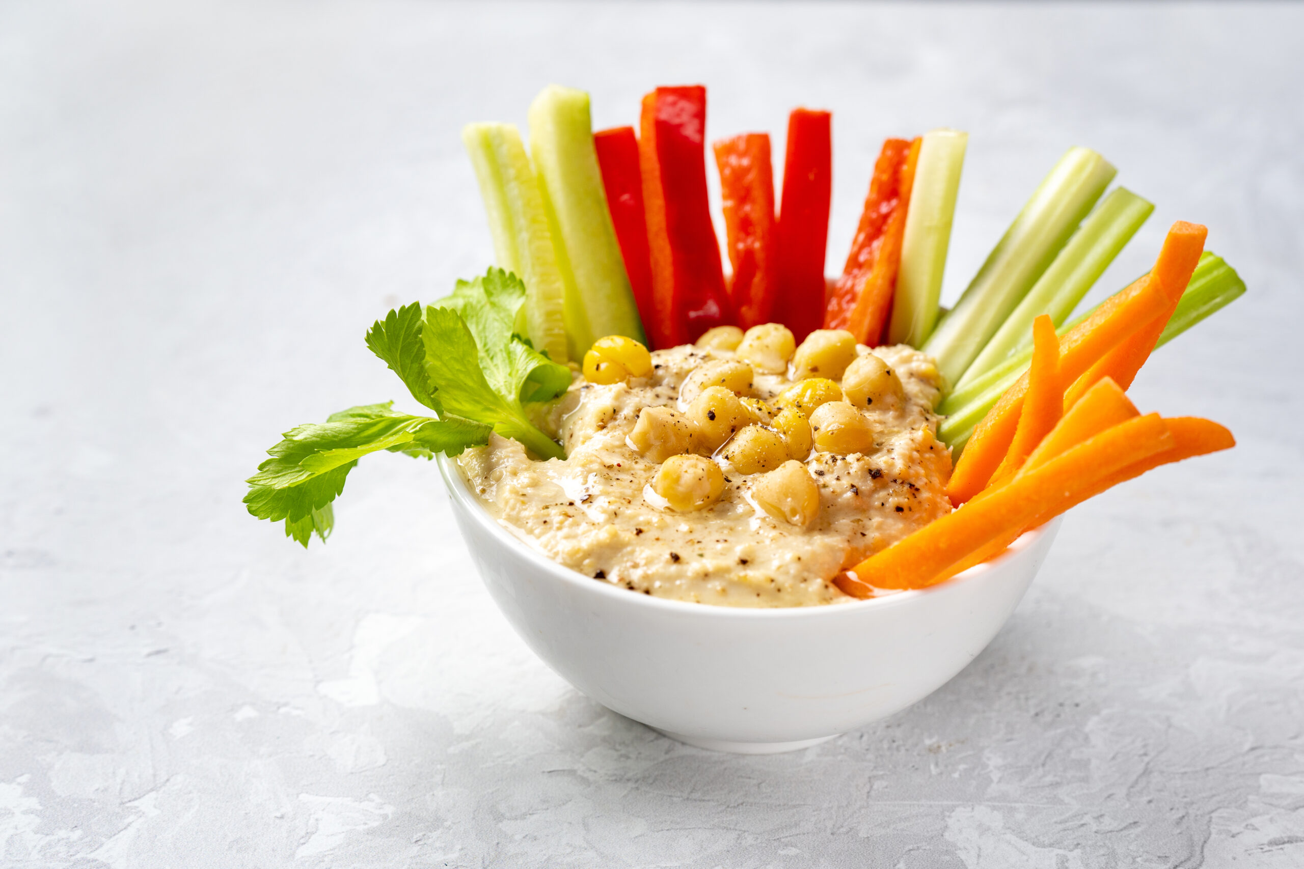 Close up of a plate with hummus dip and vegetables sticks on white background. Healthy enriched vegan food concept