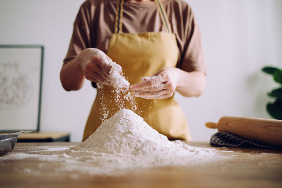 Cropped photo of an anonymous woman's hands sprinkling flour on the flour pile before kneading it.