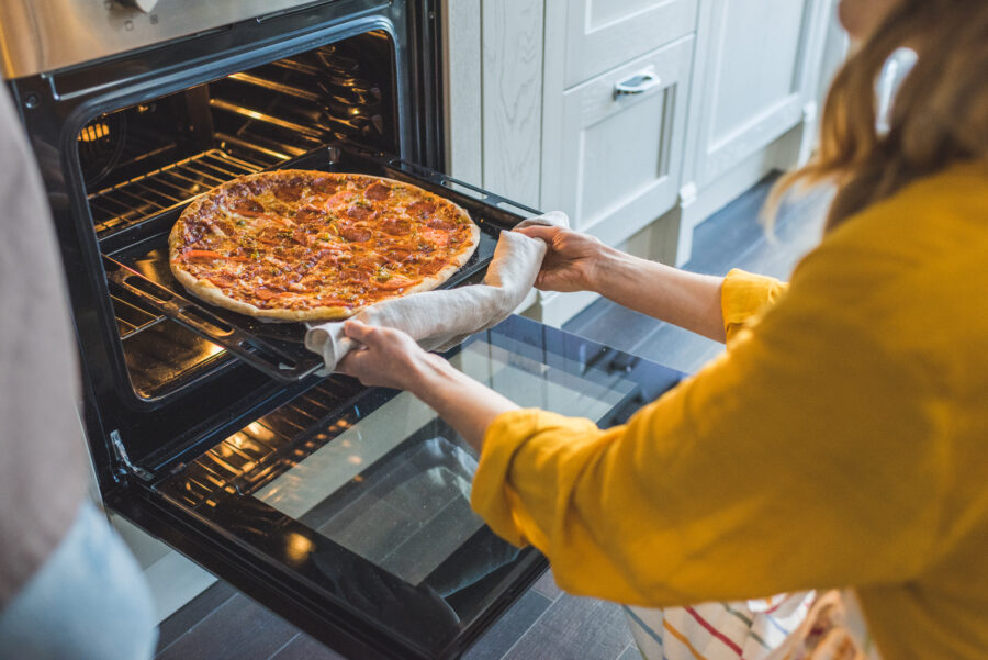 Cropped shot of young woman taking pizza from oven