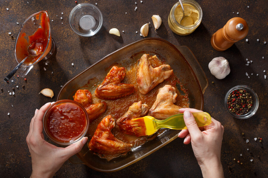 Hands brush baked wings with bbq sauce