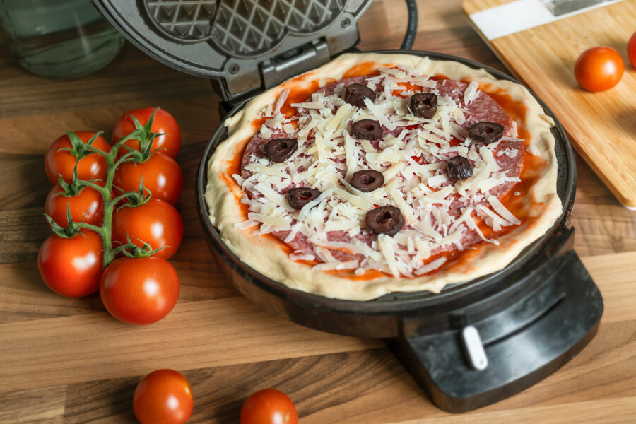 pizza waffle with pepperoni, olives and parmesan cheese ready to bake in a waffle iron