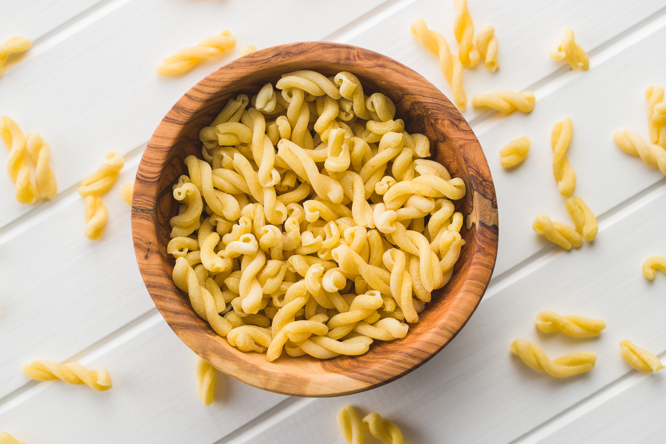 Uncooked gemelli pasta in wooden bowl.