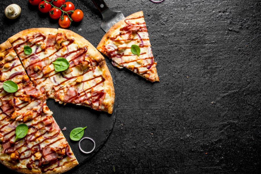 Sliced pizza with chicken, bacon and sauce. On black rustic background