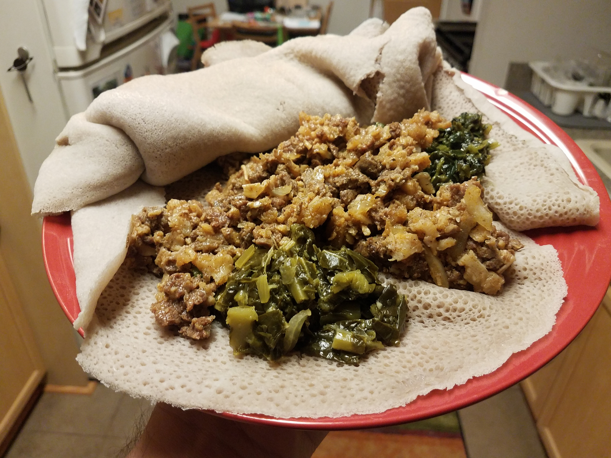 Ethiopian food beef and tripe with greens and bread on red plate in kitchen