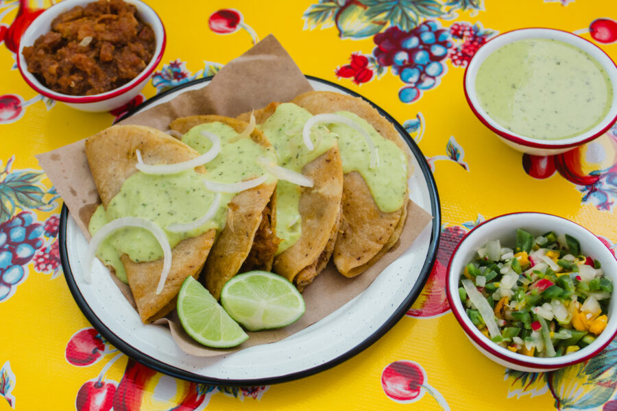 Tacos de canasta on a plate, surrounded by small bowls of sides