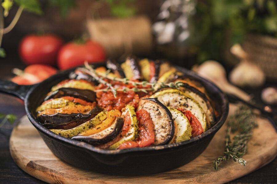 Ratatouille made of zucchini, eggplants, peppers, onions, garlic and tomatoes slices with aromatic herbs, bread. Rustic wooden table. 