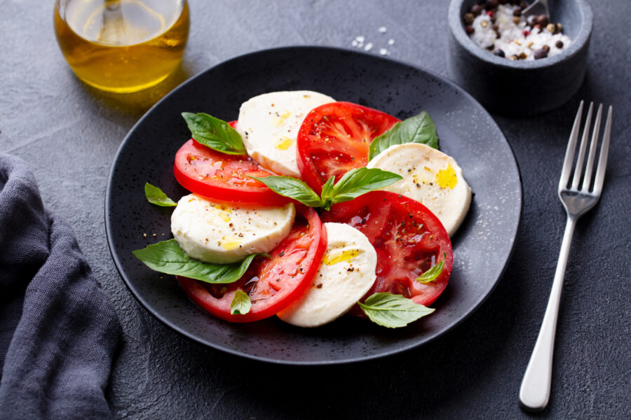 Caprese salad with tomatoes, mozzarella cheese, basil. Dark background. Close up.