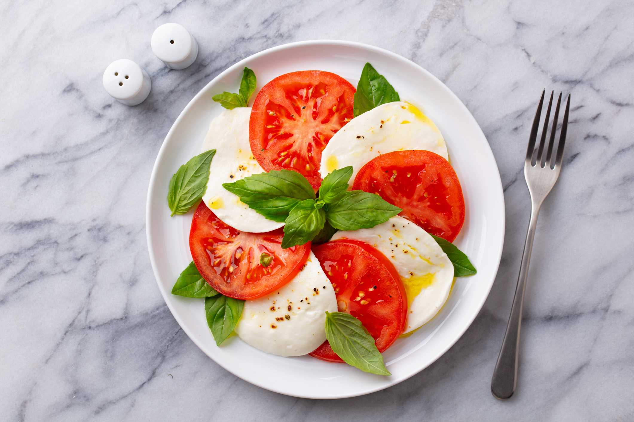 Caprese salad with tomatoes, mozzarella cheese and basil on a white plate. Marble background. Close up. Top view.