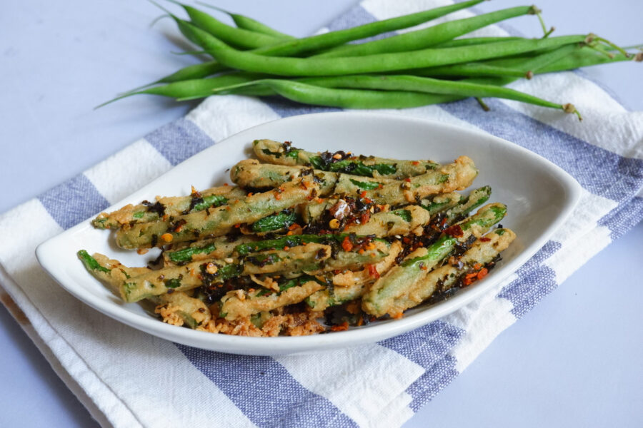 A plate of fried crispy green beans with chilli flakes  in white background