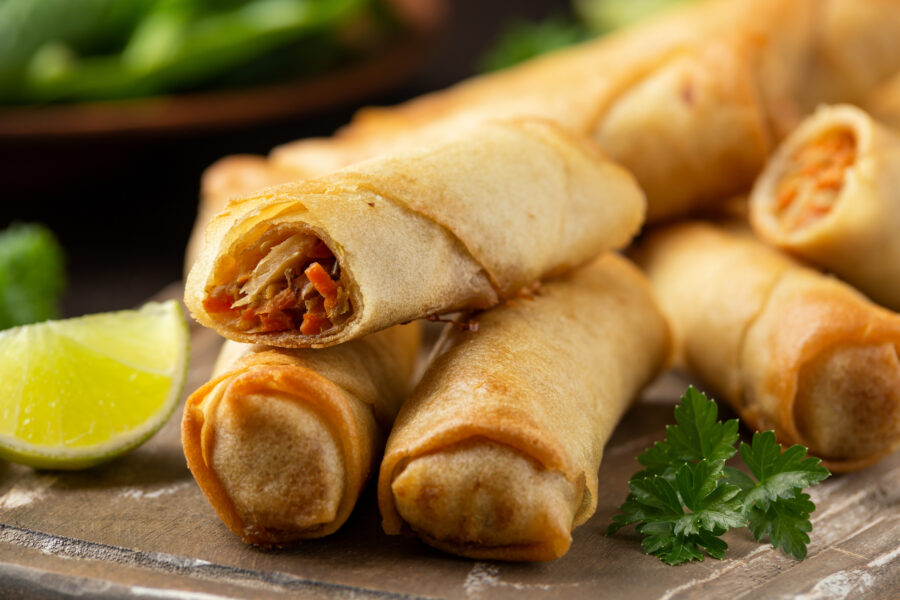 Fried vegetable spring rolls with sweet chili and soy sauce on wooden board.