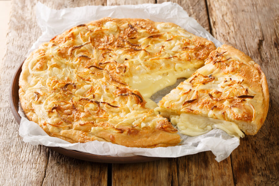 Fugazzeta Argentinian deep dish pizza stuffed with mozzarella cheese and topped with parmesan cheese and toasted onions closeup in the plate on the wooden table. Horizontal