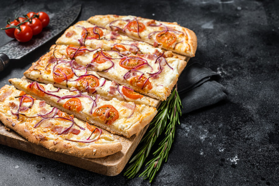 Flammkuchen or tarte flambee with cream cheese, bacon, tomato and onions. Black background. Top view.